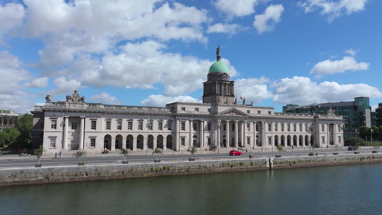 Edificio civico neoclassico con cupola in rame si erge lungo una banchina tranquilla mentre un drone scivola via in una limpida giornata estiva