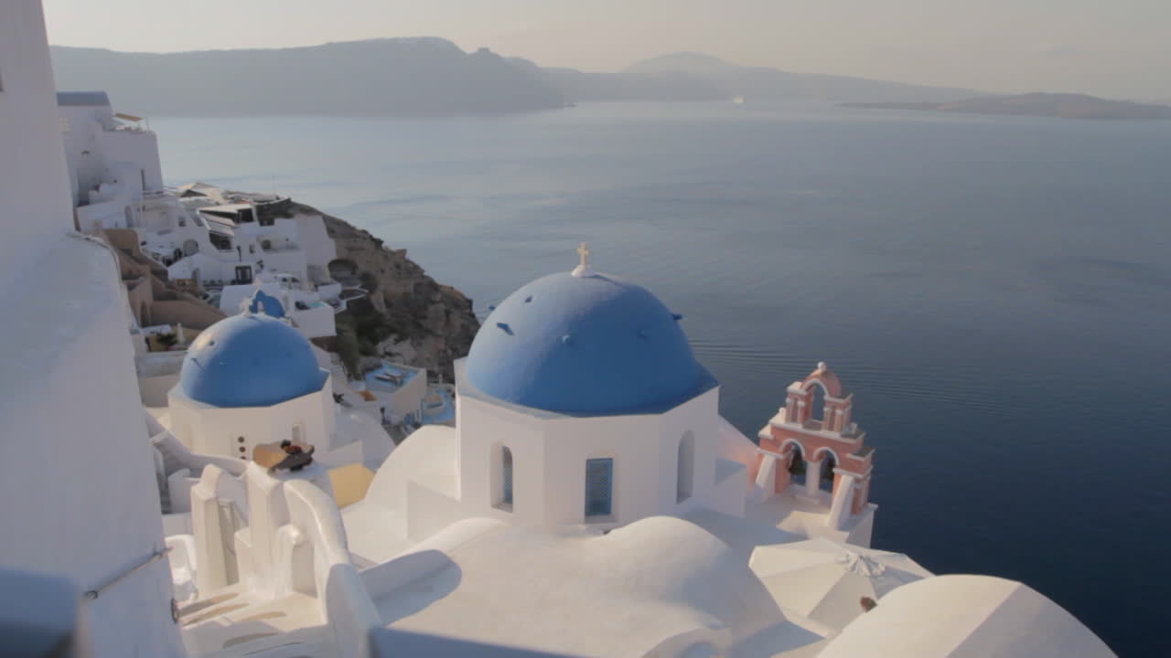 cúpulas de iglesia azul y campana de iglesia rosa con vistas a un majestuoso paisaje marino en oia, santorini