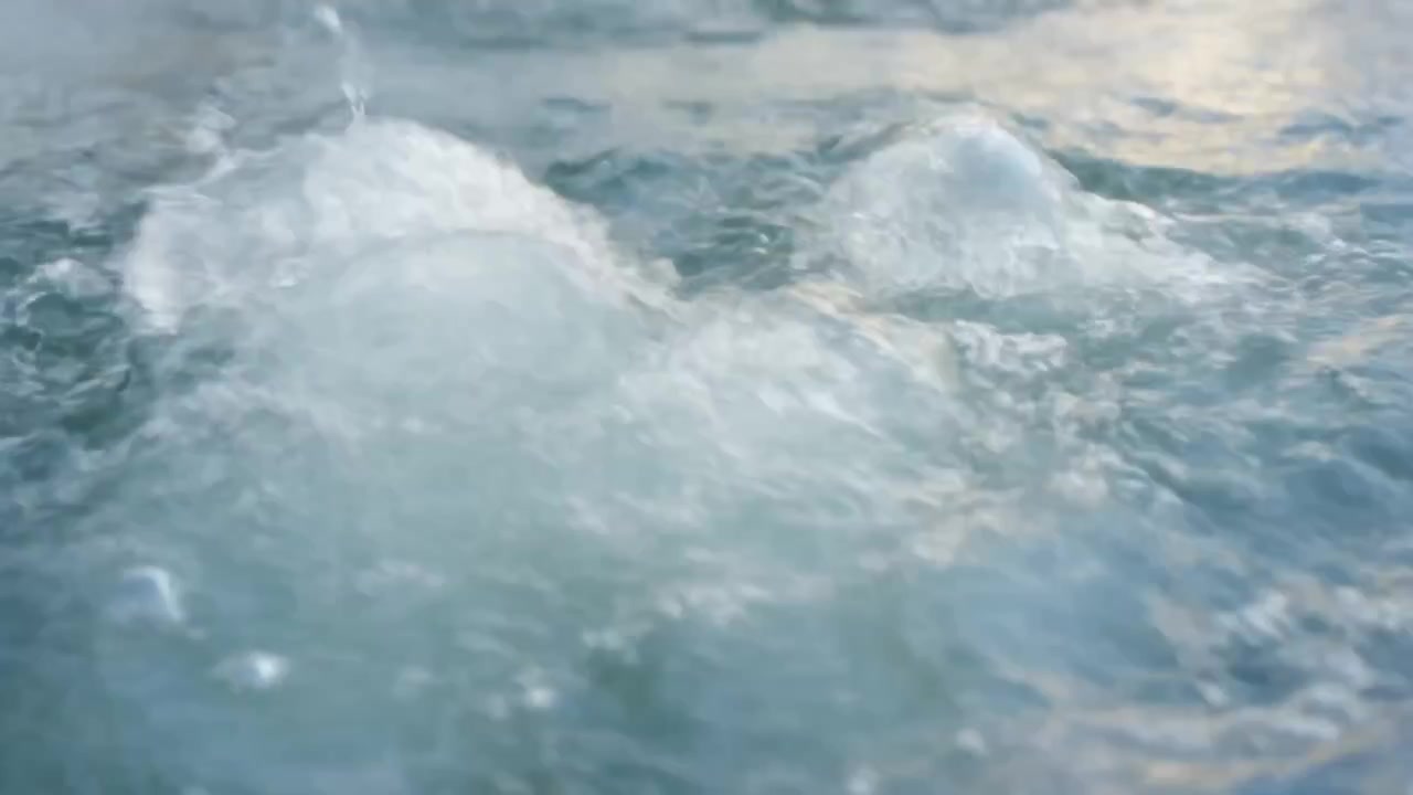 Superficie dell'acqua che ribolle in acque aperte, formando spruzzi schiumosi da un disturbo sottomarino, con luce soffusa.