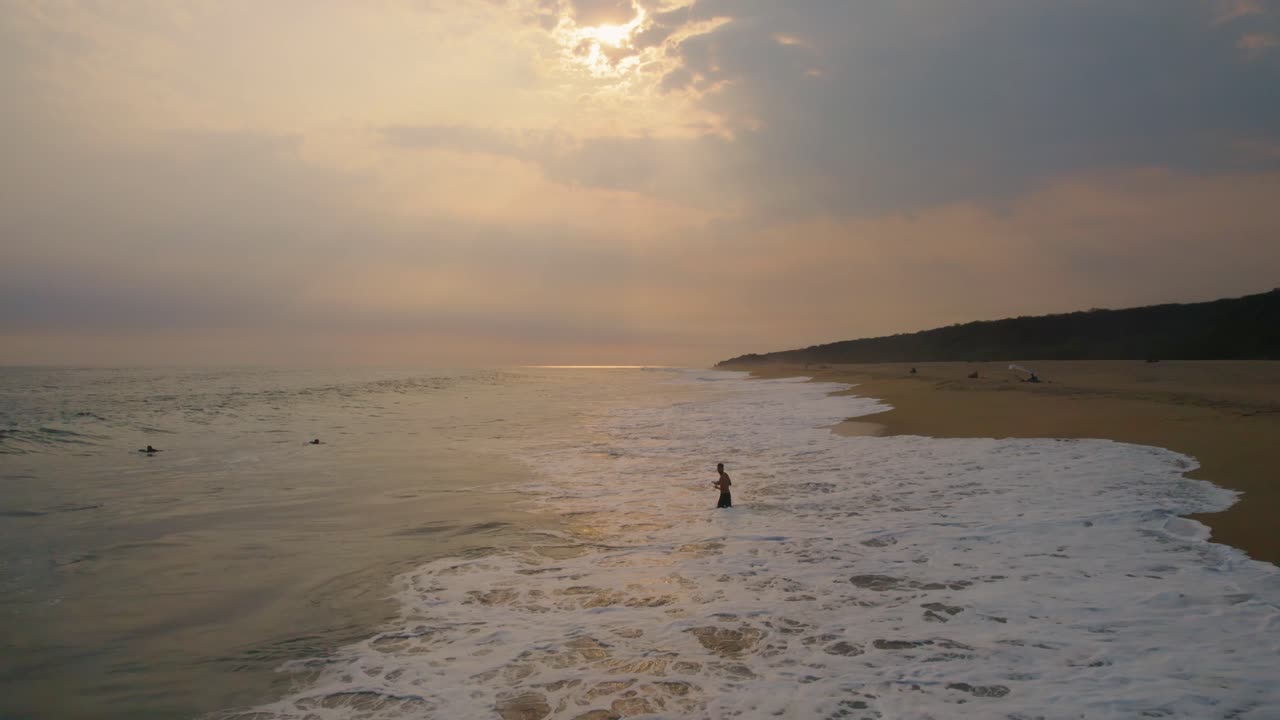 High speed backward aerial shot of a beautiful beach at sunset as a person swims in the Pacific Ocean in Oaxaca, Mexico