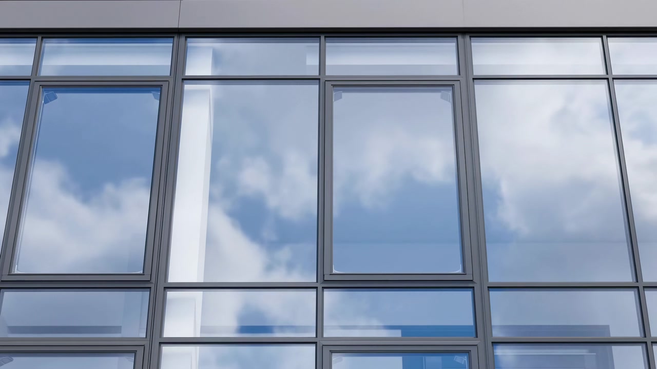 Scène frontale d'une façade de bureau moderne avec de grands panneaux vitrés rectangulaires dans des encadrements en métal foncé, montrant de subtils reflets changeants du ciel et des nuages sur chaque vitre sous une lumière urbaine claire