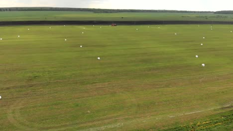 aerial: landscape with a tractor on a hay field collecting fresh grass with a coil wrapper
