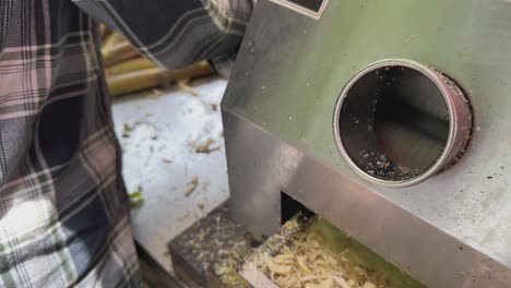 closeup of hand guides the sugarcane into the machine, while the rollers begin the juicing process