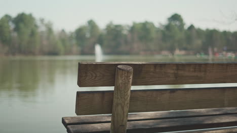 left side of a wooden bench in front of a lake with a water fountain in the middle