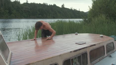 fit young man topless sanding timber roof planking of old wooden boat