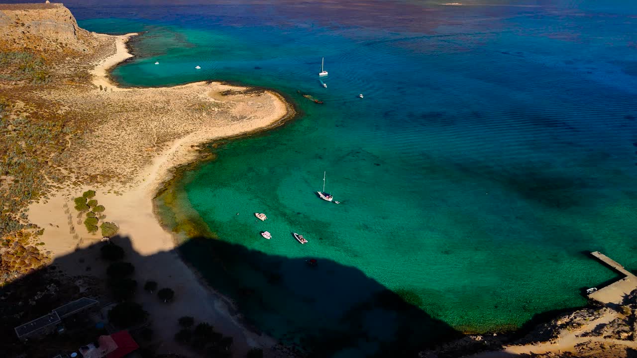 Breathtaking views of a serene bay show the clear blue sky above calm waters. The rocky coast and gentle waves create a peaceful atmosphere in Crete, Greece