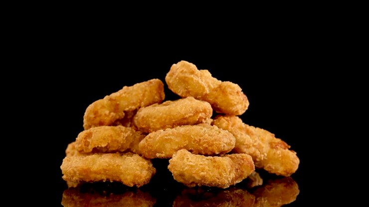 Golden breaded chicken nuggets rotate in slow motion against a glossy black surface, with dramatic studio lighting highlighting texture and color in a seamless loop