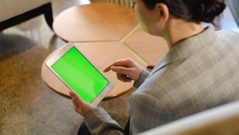 young business woman using tablet device with green screen. woman holding tablet, scrolling pages. view over shoulder.