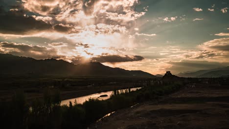 setting sun and moving rays of light silhouetting stakna monastery on the indus river, leh ladakh