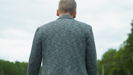 an upward view of an aged man in jeans and canvas shoes walking calmly on rocky railway tracks, with trees around and sky in view