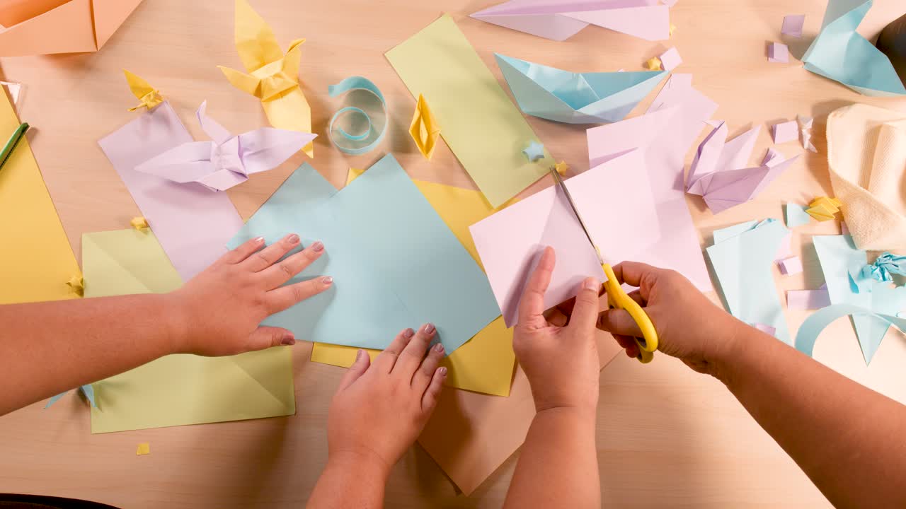 Two people cut colored paper for origami on a tidy table under soft, even lighting