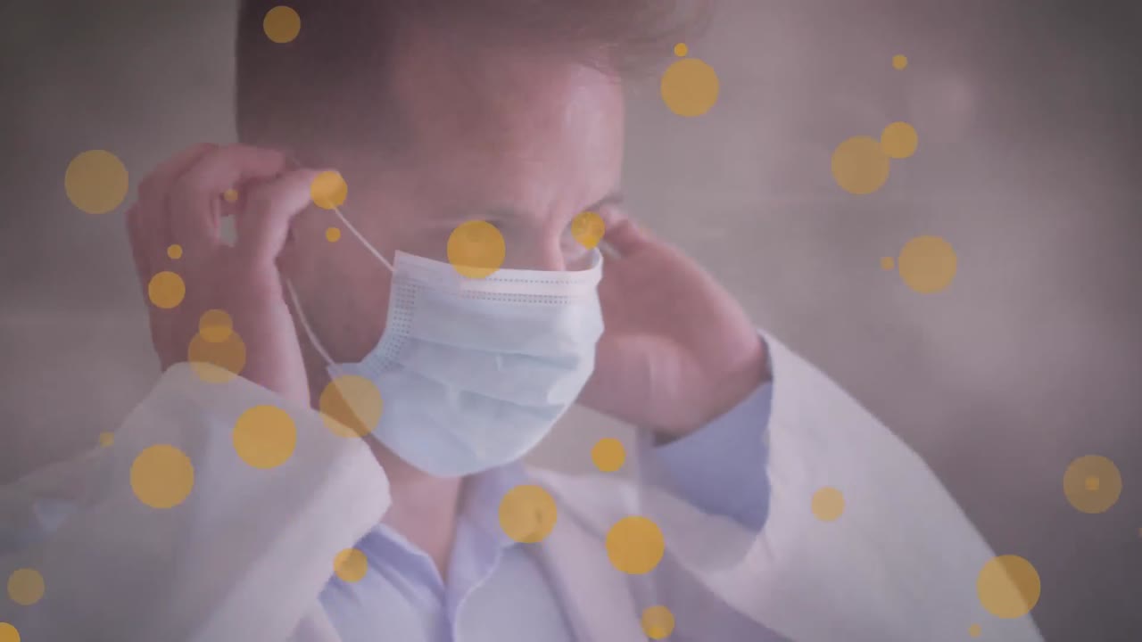 フェイスマスクを着けた白人男性医師の上に黄色い斑点と光の点々が重なるアニメーション