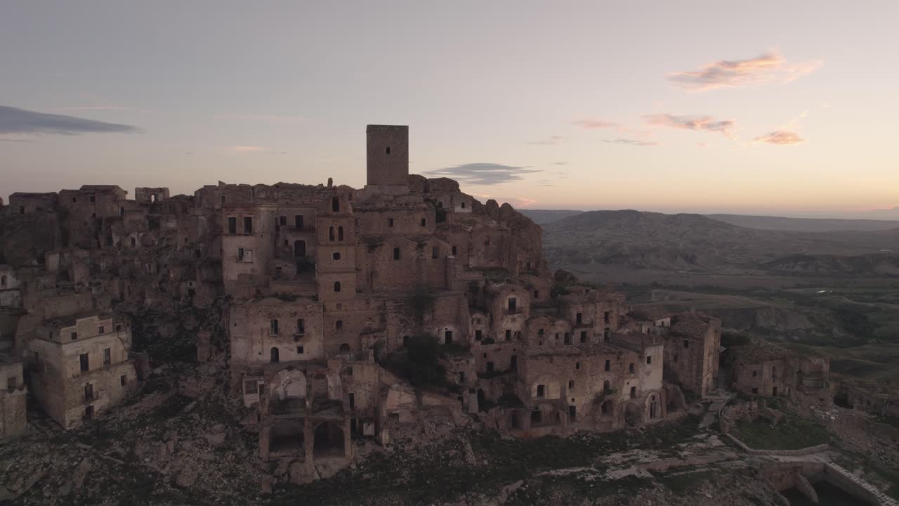 Drone flying backwards away from the ruins of Craco on a hill in the south of Italy at sunrise in 4k