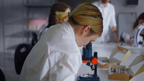 A woman in a lab coat looks through a microscope in a laboratory.