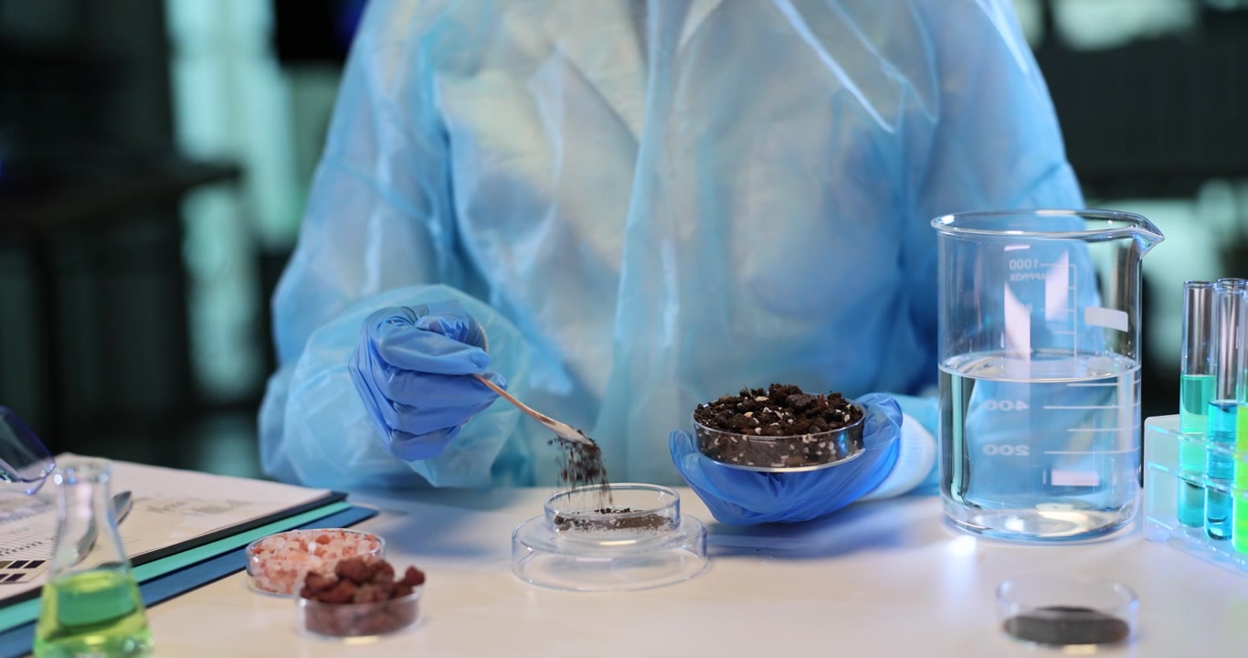 Lab assistant transfers dry brown soil into transparent container