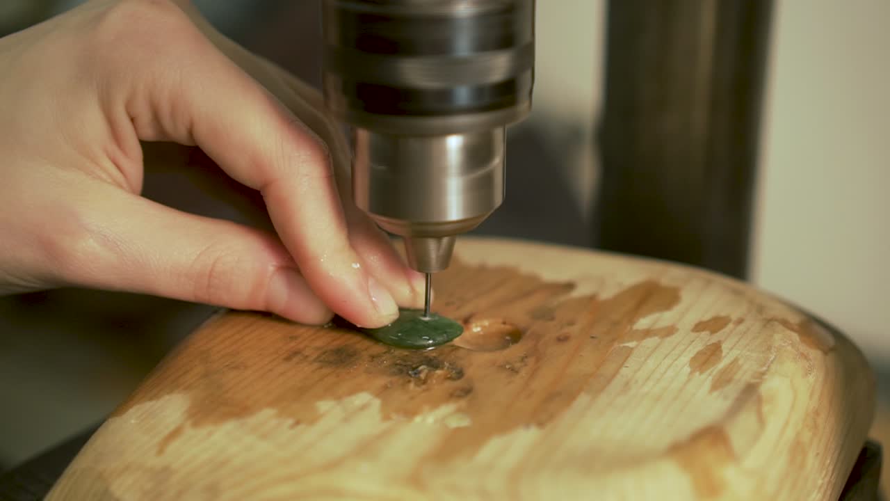 Dettaglio della perforazione di un piccolo foro nella pietra verde della Nuova Zelanda, su lastra di legno al rallentatore