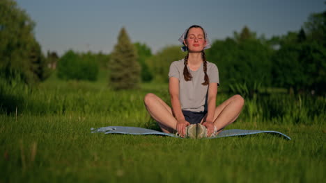 a young woman settles on her yoga mat in a sunlit park as the camera pulls back, capturing her peaceful energy and the beauty of golden hour in nature.
