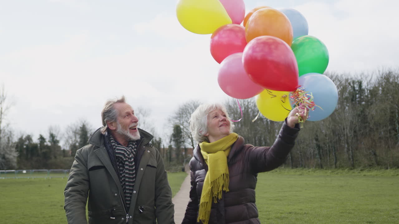 amorosa pareja de ancianos con globos disfrutando del otoño o el invierno caminando juntos por el parque
