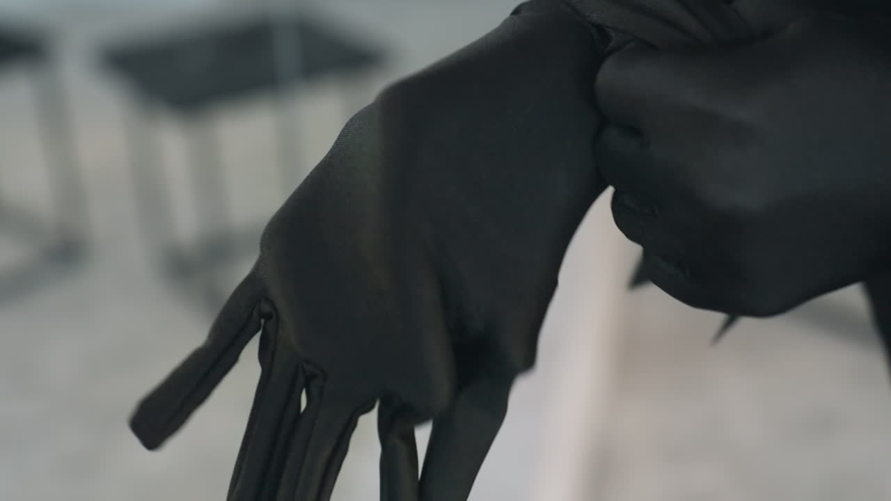 close up of person sliding on smooth black glove over fingers and hand, soft folds of fabric visible, muted studio background slightly blurred for dramatic focus on elegant motion and texture