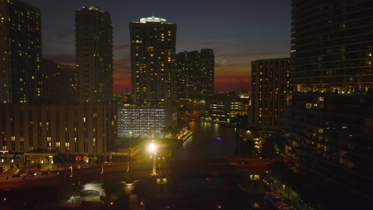 hacia adelante volar sobre el puente que atraviesa el río que fluye entre los edificios altos del centro de la ciudad. escena nocturna de la ciudad. miami, ee.