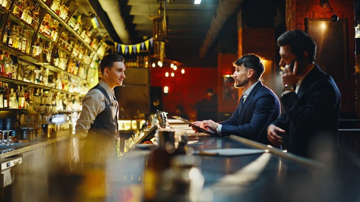 Uomini che salutano l'addetto al bar ordinando da bere la sera. Clienti allegri che si divertono.
