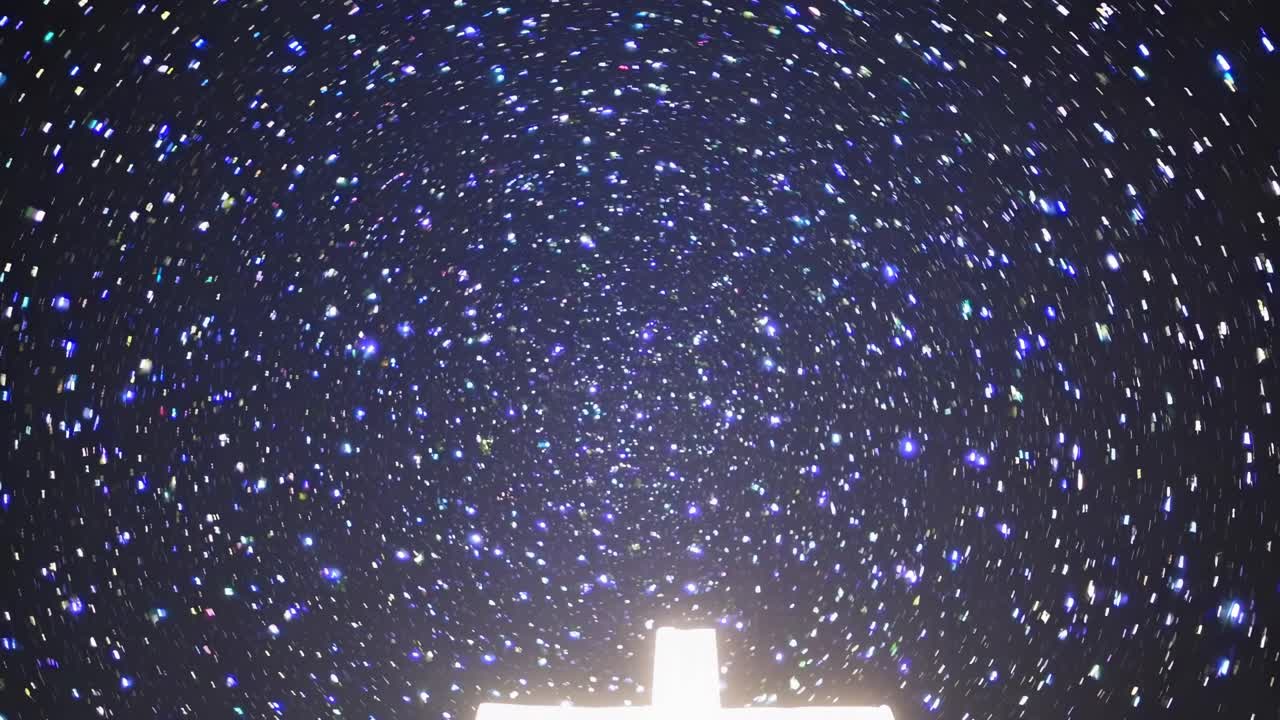 A mesmerizing video of a starry night sky captured from a low angle, focusing on a glowing cross