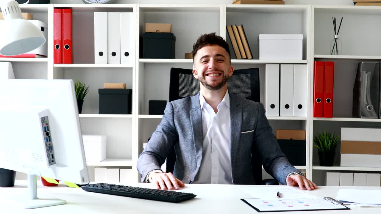 uomo d'affari in giacca grigia seduto a tavolo in un ufficio bianco e rallegrandosi del successo