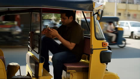 man using phone in auto-rickshaw on street