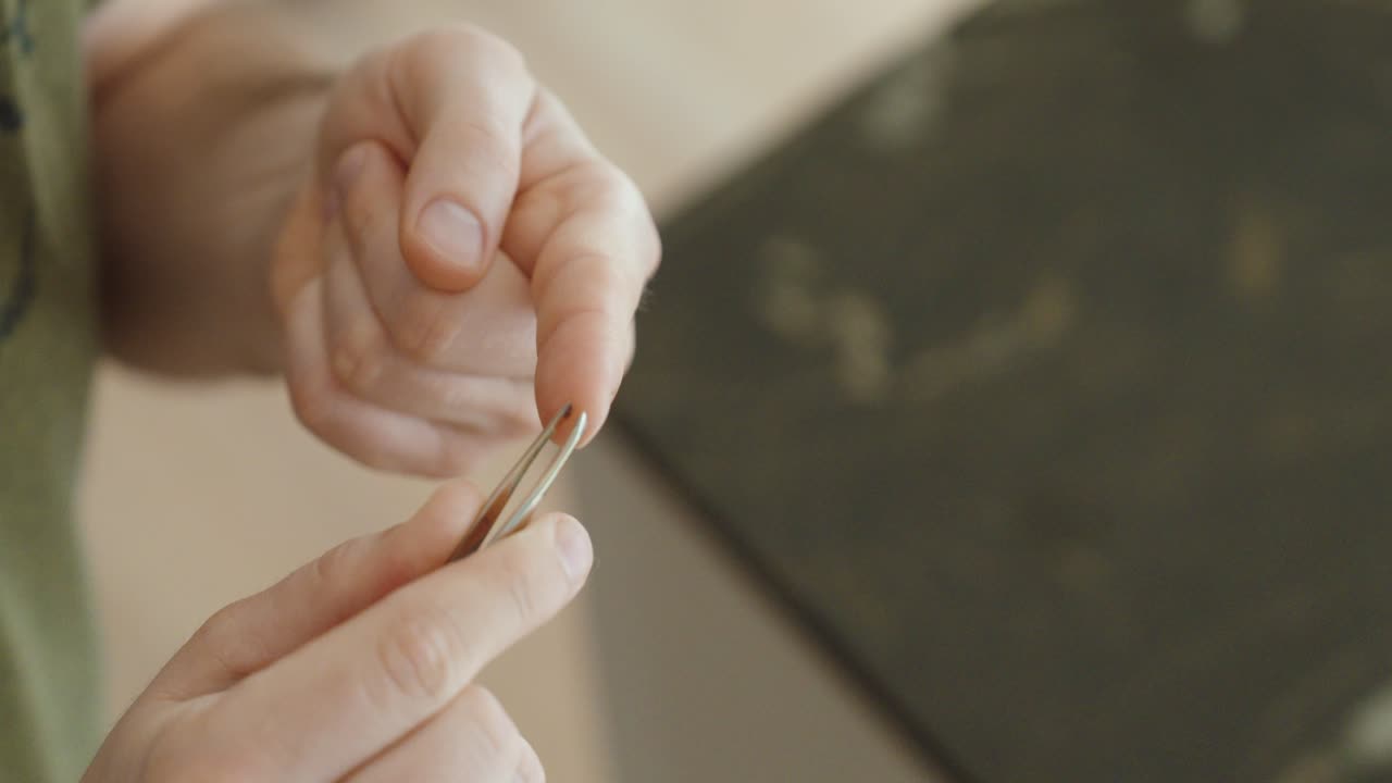 Careful removal of a small splinter from a fingertip using tweezers at home, demonstrating gentle handling, attention to detail, and basic personal care in a calm indoor setting