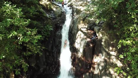 Panning-Down-Drone-shot-following-someone-going-down-the-natural-waterslide-at-AlingAling-Waterfall-in-Bali,-Indonesia