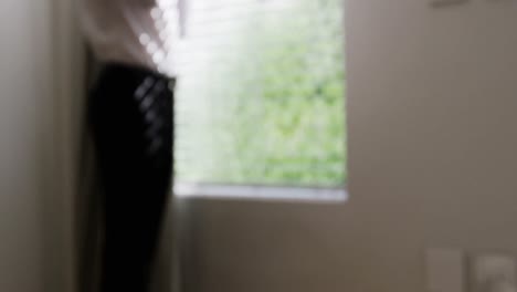 man getting dressed while looking through window in bedroom