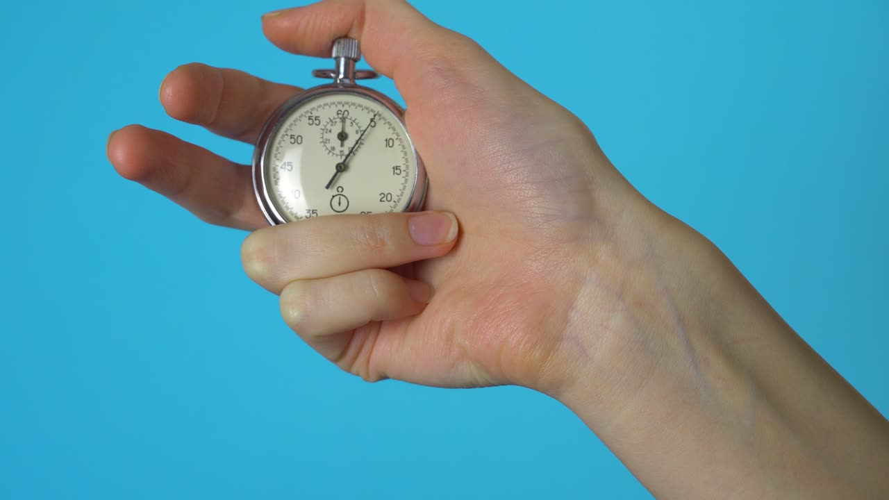 A woman's hand holds an analog stopwatch on a blue chromakey screen.