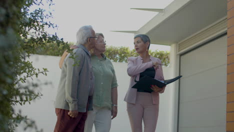 female real estate agent standing in the backyard and showing the property to a senior couple