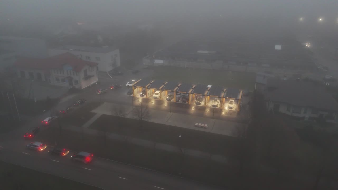 Glowing lights of car wash and huge vehicle line with dense fog, aerial view