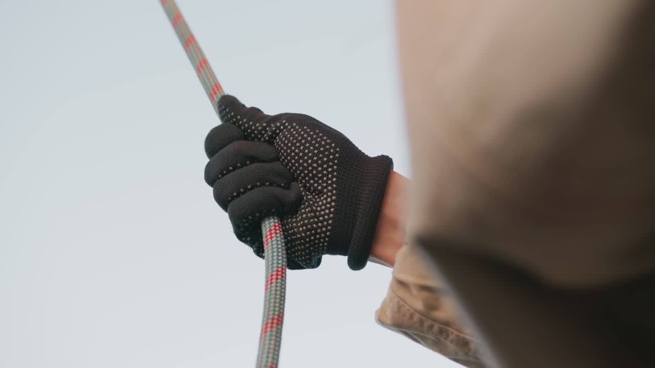 close up of person wearing black grip glove tightly holding colorful safety rope during outdoor activity showing strength control and readiness under clear sky background