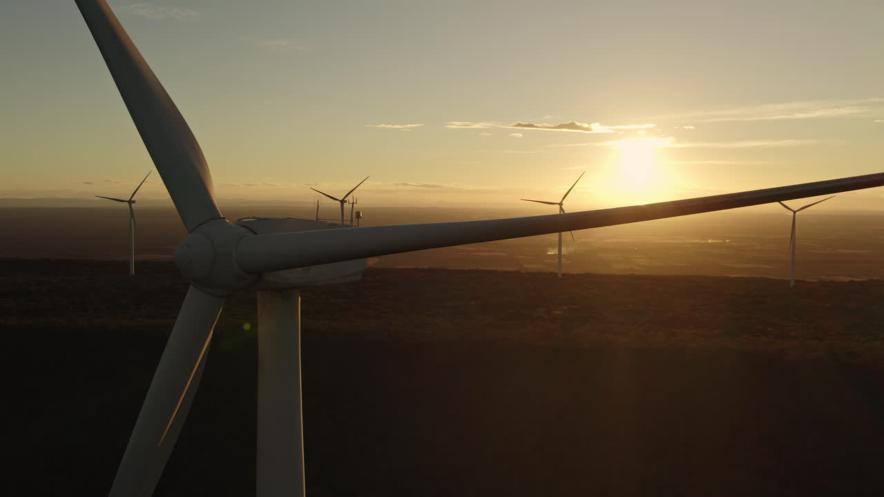 Aerial going up shot with golden Sunset view with wind turbine towers in the background and a big one in the close up shot, Alternative energy source