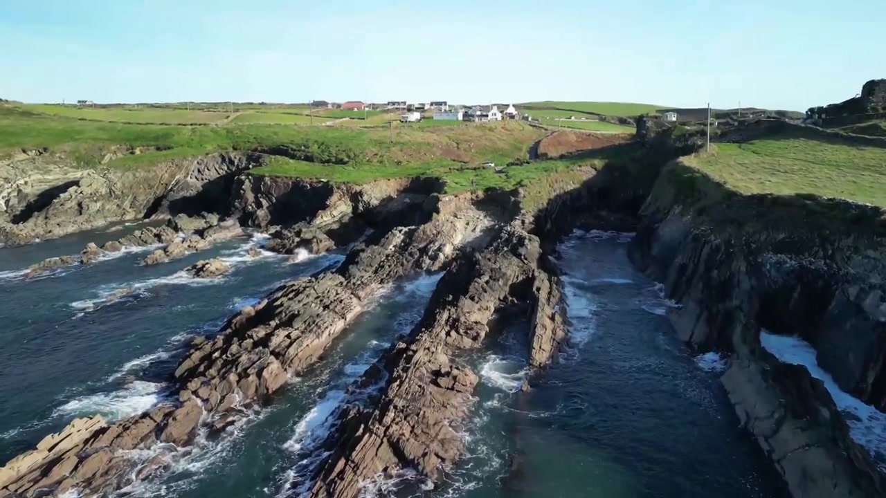 Drone flyver lavt og tæt over klipper og bølger, der afslører en barsk kystlinje i Irland.