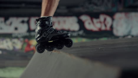 junger rollschuhfahrer, der an einer rampe im skatepark mit graffiti-wand übt.