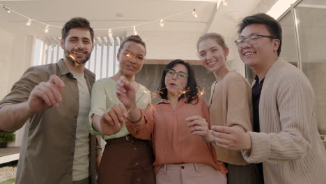 a multiethnic group of friends looking at the camera, smiling and shaking some sparklers