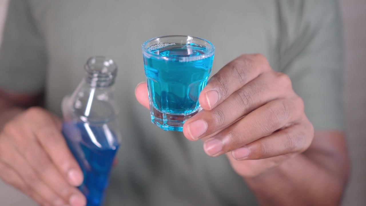 Persona sosteniendo un vaso de chupito lleno de líquido azul