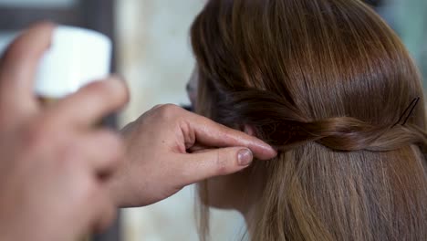 hairdresser creating a hairstyle for bride in salon using spray lacquer fixing