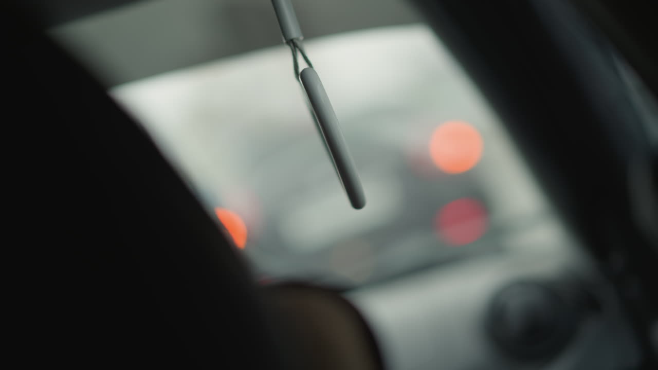 Interior car cabin shot with dutch angle capturing heart shaped handle hanging by window in motion against blurred urban background under overcast winter sky conveying subtle atmosphere