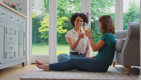 same sex female couple or friends at home relaxing in lounge drinking wine together