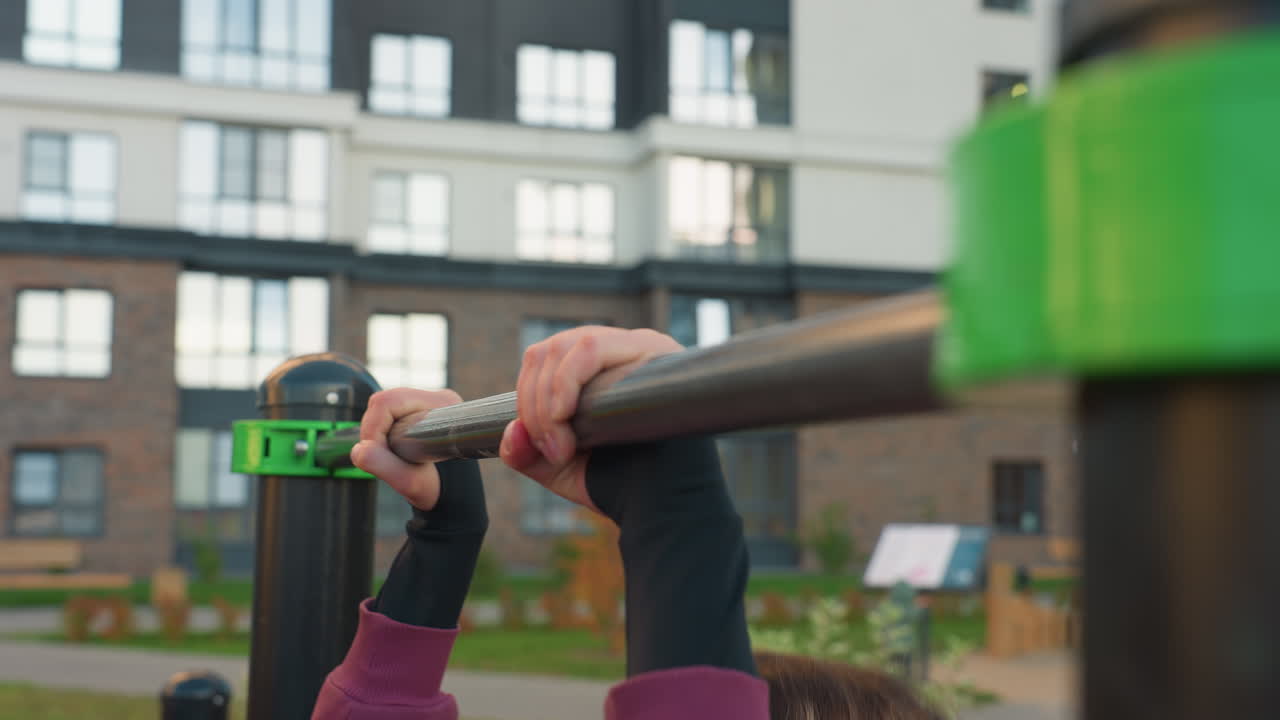 Side view of female instructor hands gripping horizontal pull up bar in urban park gym against city backdrop exhaling to maintain balance, forearm strength control and intense calisthenics focus