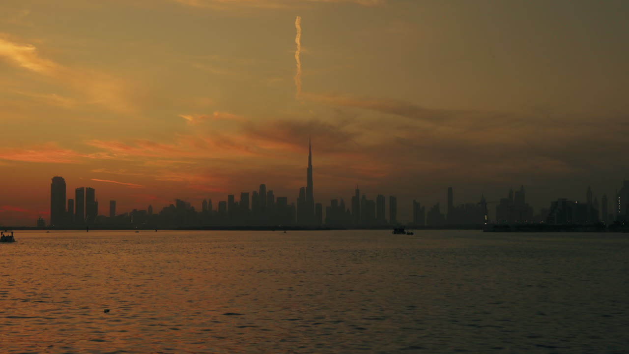 Vista dello skyline cittadino al tramonto dal porto di Dubai Creek, grattacieli futuristici, cielo desertico vibrante e barche