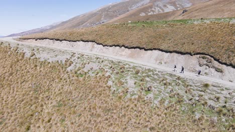 Three-hikers-making-their-way-up-a-side-of-a-dry-mountain-in-sunshine