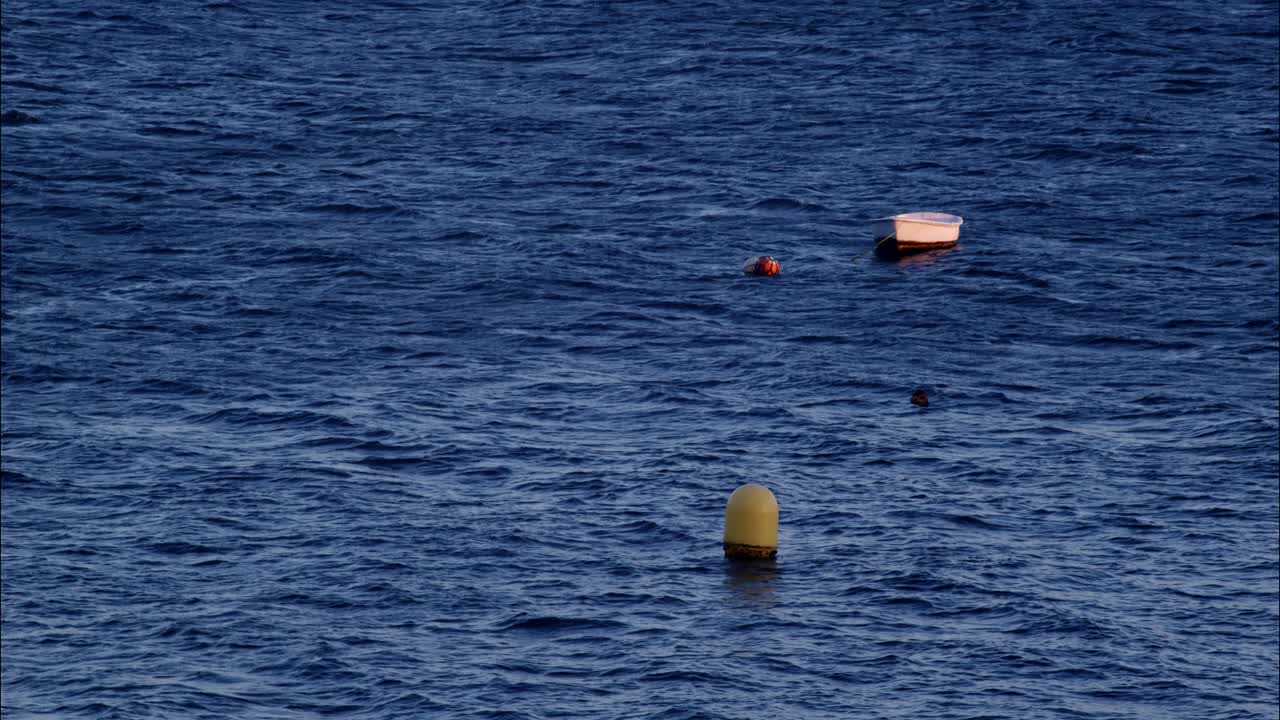 Small White Boat and Buoys Floating on Dark Blue Ocean