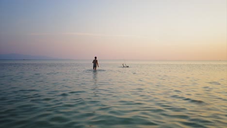people in the ocean at sunset, possibly fishing