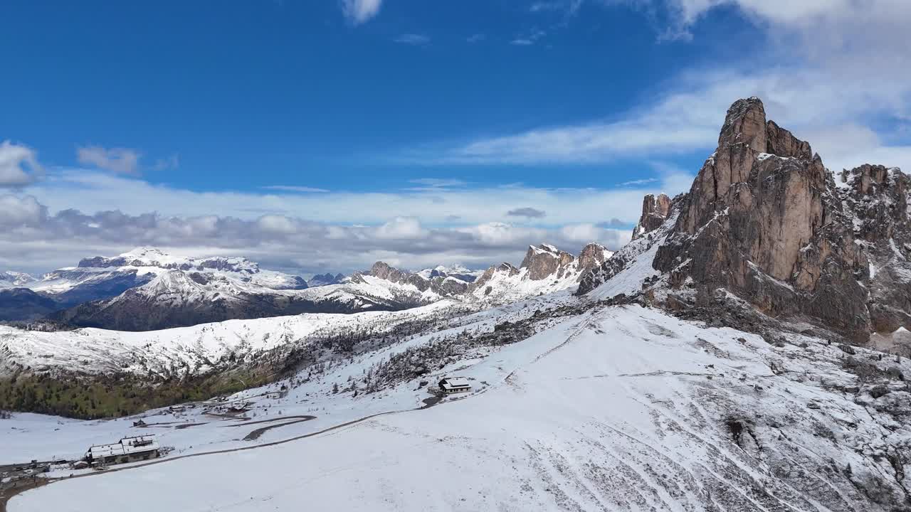 Drone video of snowy mountains in Passo Giau with blue sky and clouds