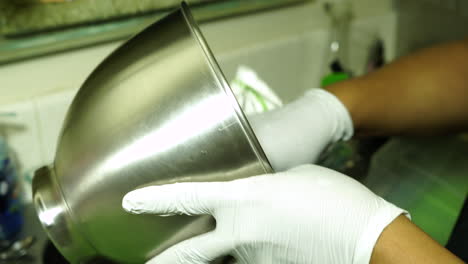 persona con guantes blancos está secando un tazón mezclador de acero inoxidable